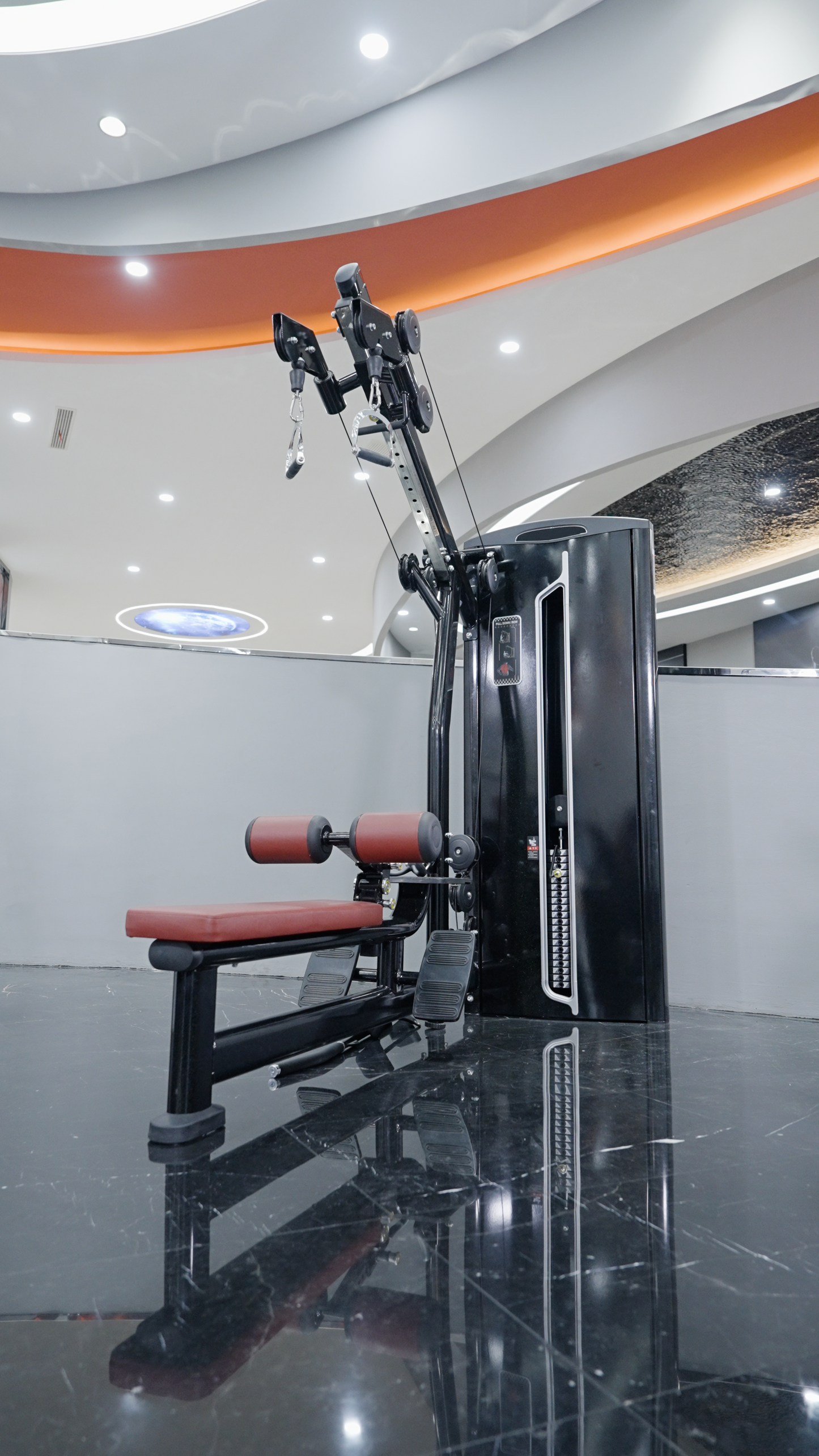 The BefitNow Canada Iso Lateral Lat Pulldown/Low Row, featuring black and red padding and a weight stack, stands on a shiny black floor in a brightly lit, modern gym with curved ceiling accents.