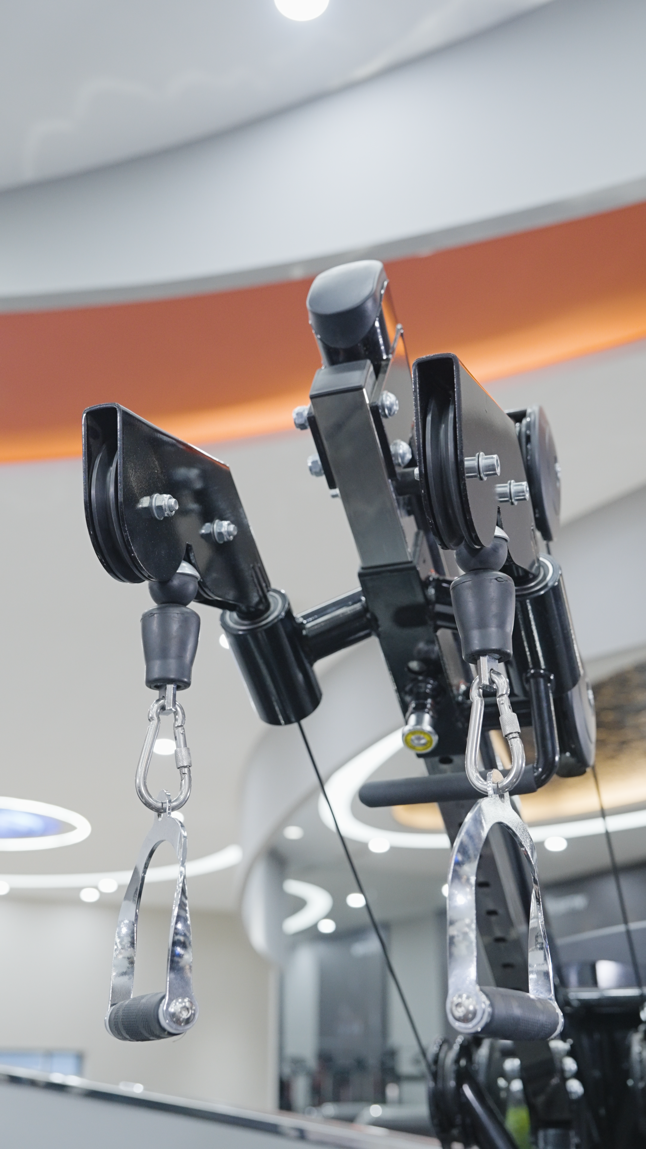 Close-up of the BefitNow Canada Iso Lateral Lat Pulldown/Low Row machine’s handles, pulleys, and weight stack with a modern gym interior blurred in the background—perfect inspiration for your home fitness setup.