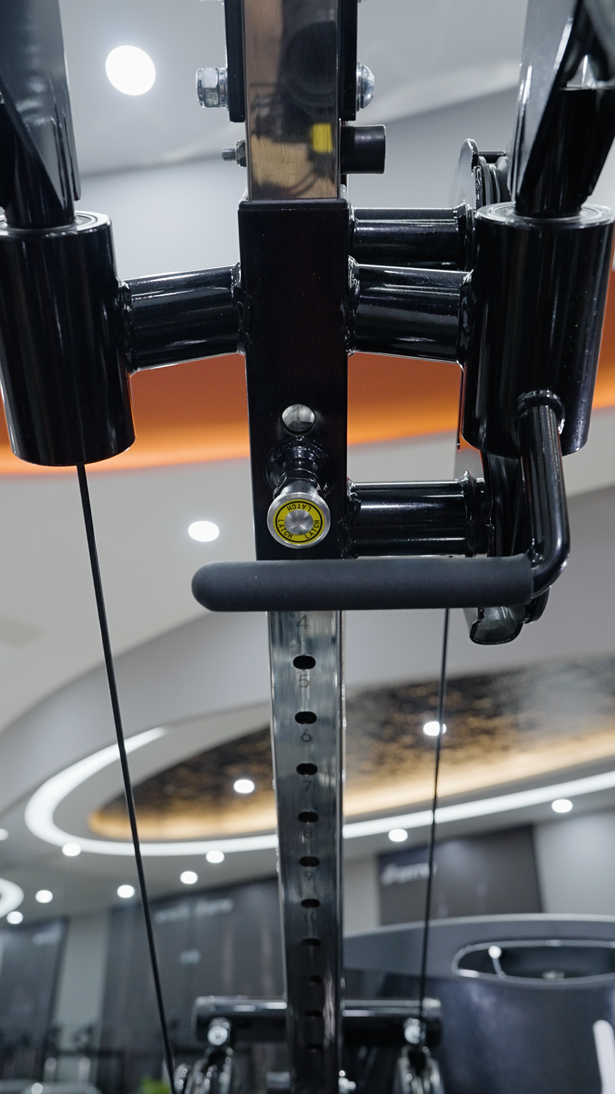 Close-up of a black BefitNow Canada Iso Lateral Lat Pulldown/Low Row machine, featuring metal parts and cables in a modern gym with curved ceiling lights and blurred background, highlighting commercial-grade quality.