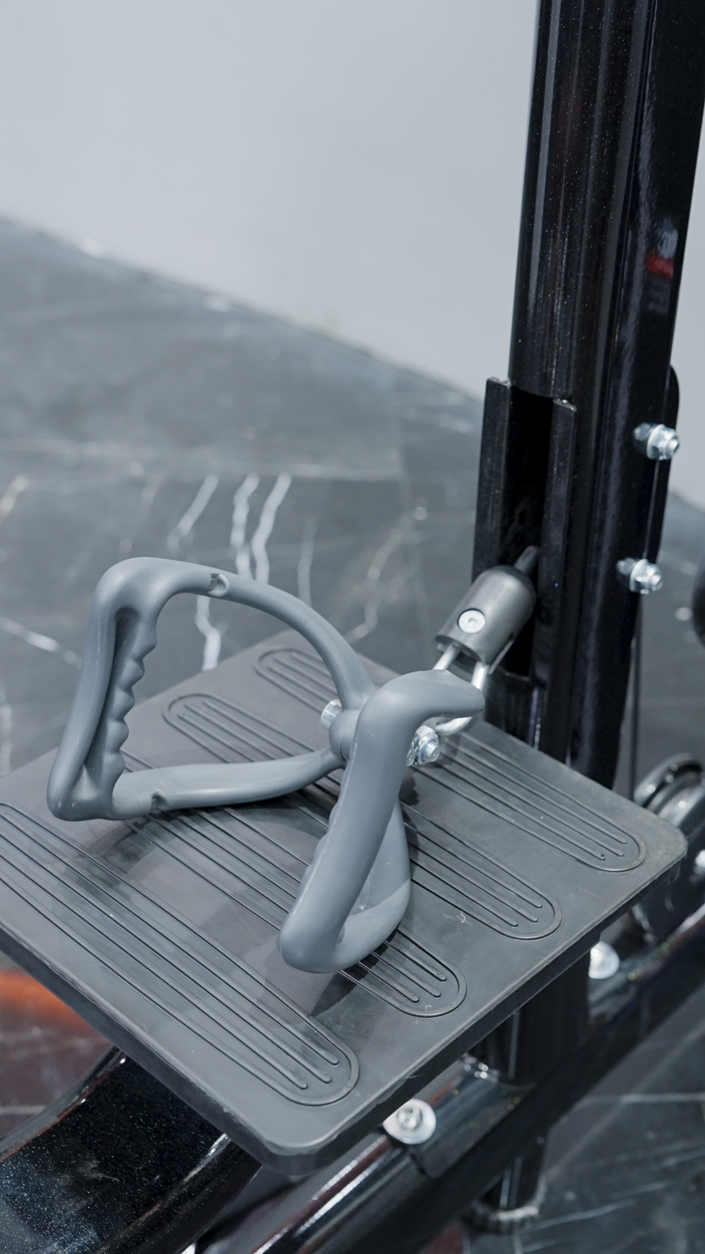 Close-up of the BefitNow Canada Iso Lateral Lat Pulldown/Low Row's textured gym machine footplate with gray rubber handles, shown on a dark marbled floor as part of its black metal home gym frame.