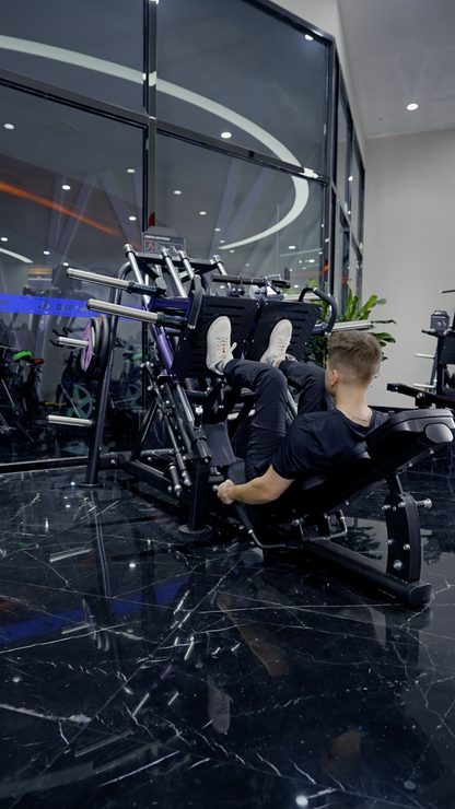 A man in black athletic wear trains his lower body at night on the BefitNow Canada Quadzilla Commercial ISO Leg Press in a modern gym with black marble floors and large glass windows.