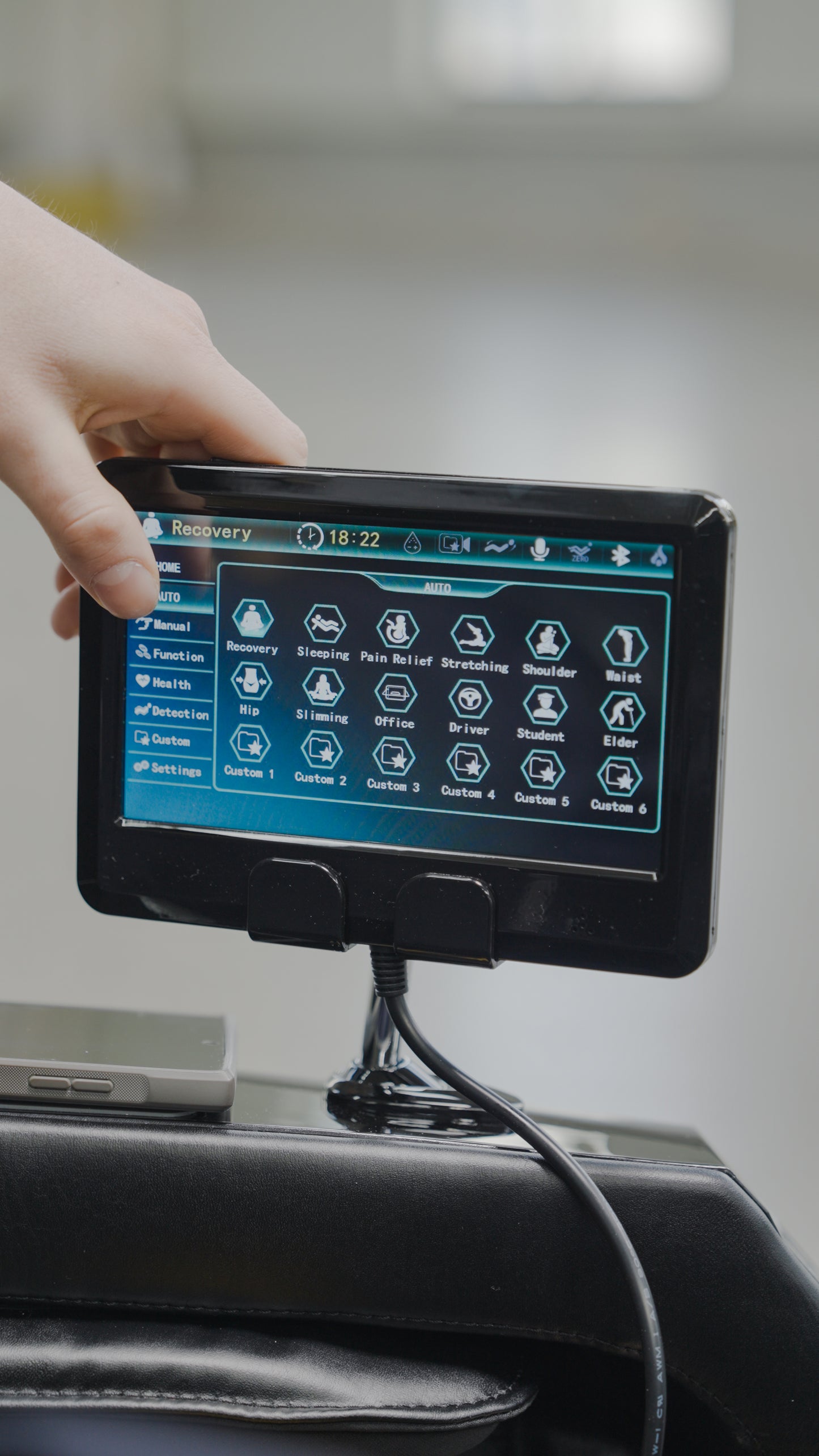 A person’s hand holds a tablet showing a recovery and therapy control interface for the BefitNow Canada 4D SL Luxury Voice Control Custom Massage Chair, featuring icons and options to enhance medical or rehab device settings.