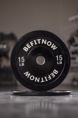 Close-up of a BefitNow Canada Bumper Plate upright, showing BEFITNOW and 15 LB in white, perfect for Olympic weightlifting. Another plate lies flat in the background, crafted for excellent shock absorption.