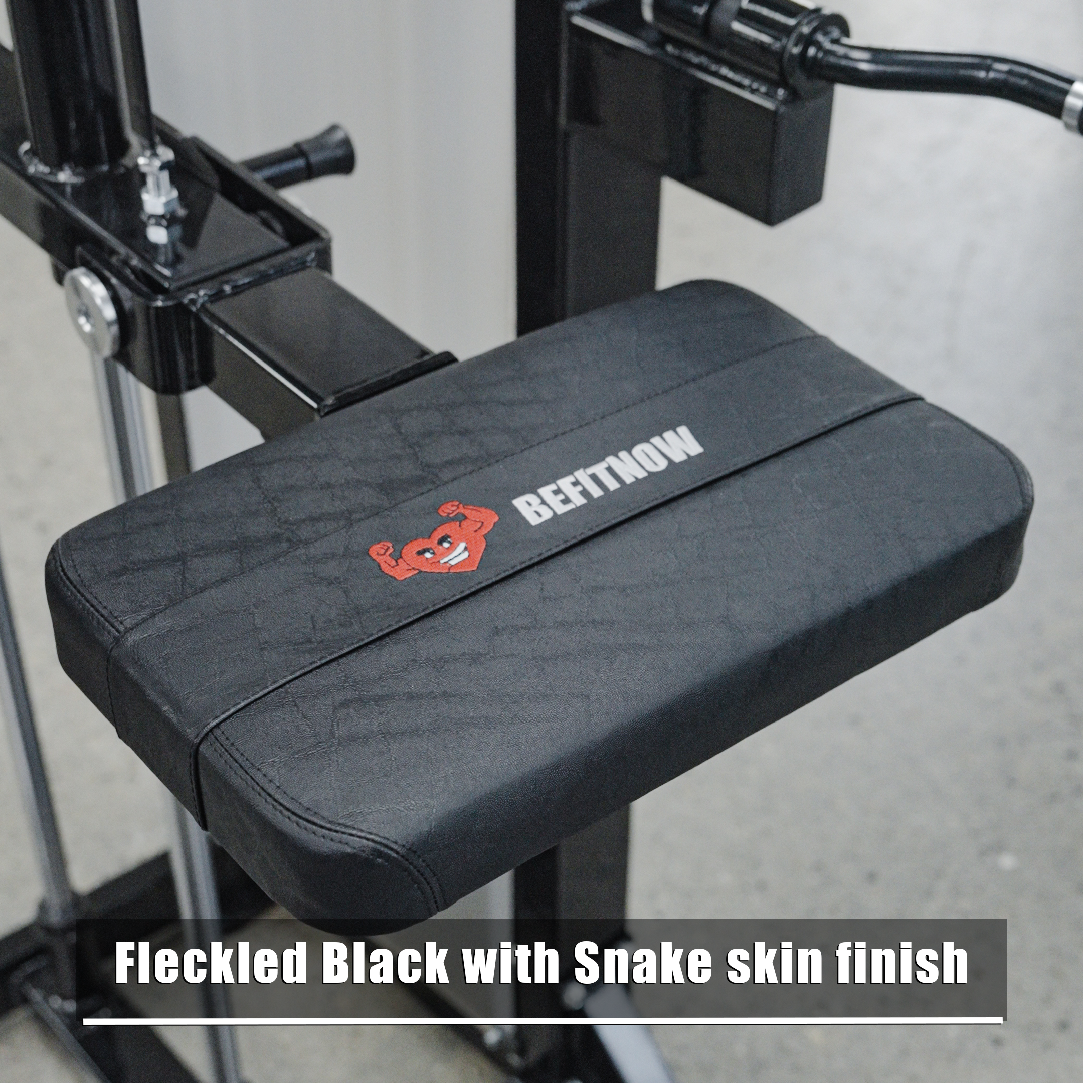 A close-up of a black padded seat with a snake skin finish, showing the BefitNow Canada logo and a red smiling crab—part of the Dip/Chin Assist machine, perfect for upper-body strength. Text below: Fleckled Black with Snake skin finish.