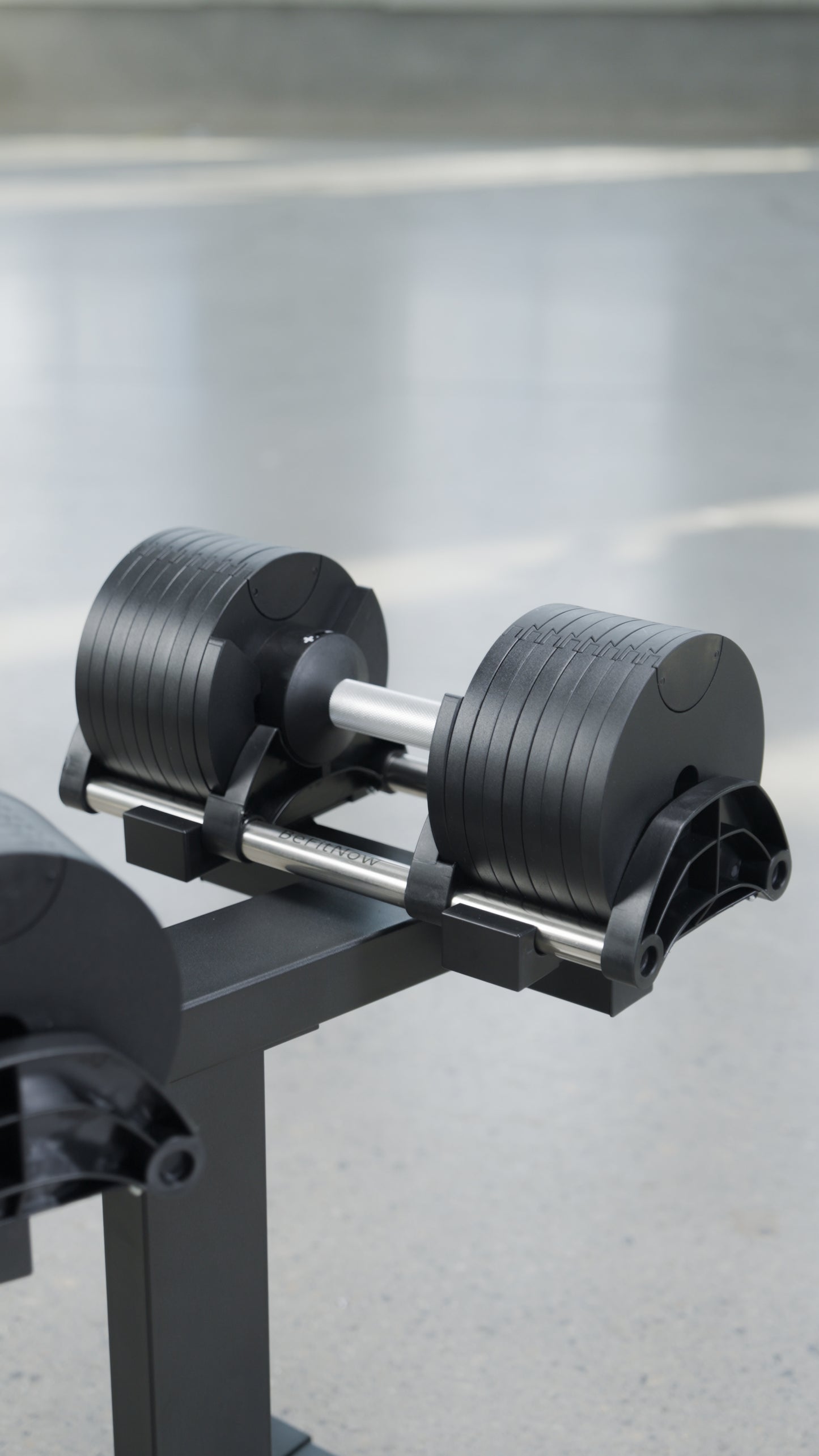 The BefitNow Canada 90lbs Adjustable Cast Iron Dumbbell Pair sits on a black stand, providing a space-saving home gym solution with multiple weight plates, set against a blurred light gray background.