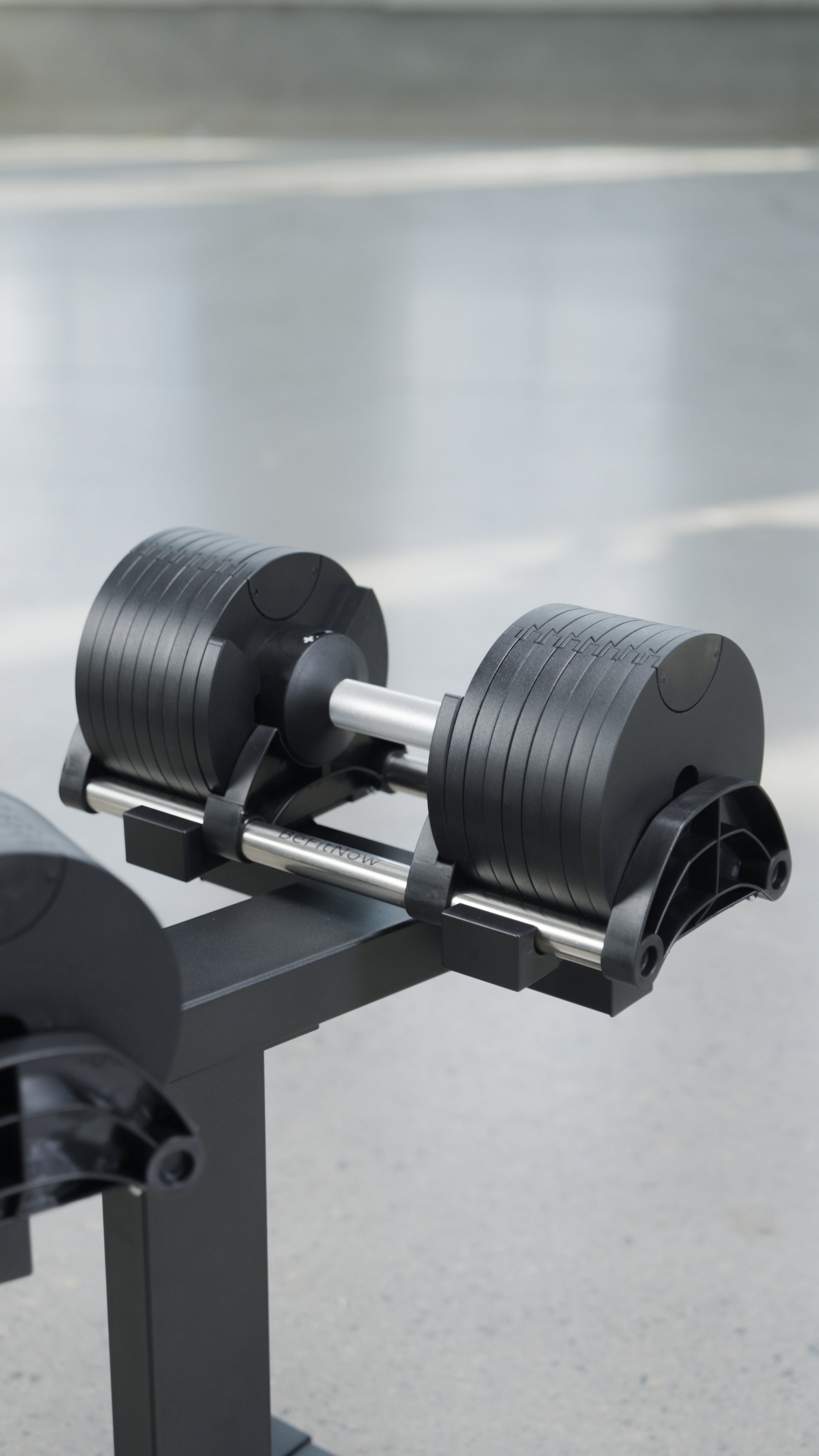 The BefitNow Canada 90lbs Adjustable Cast Iron Dumbbell Pair sits on a black stand, providing a space-saving home gym solution with multiple weight plates, set against a blurred light gray background.
