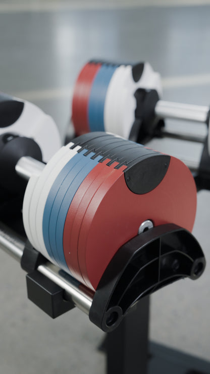 The BefitNow Canada 80lbs Adjustable Cast Iron Dumbbells, featuring colored weight plates in red, blue, and white, are displayed on a black metal rack in a gym setting. The softly blurred background highlights the sleek and functional design of these adjustable dumbbells, making them an excellent space-saving choice for your home gym.