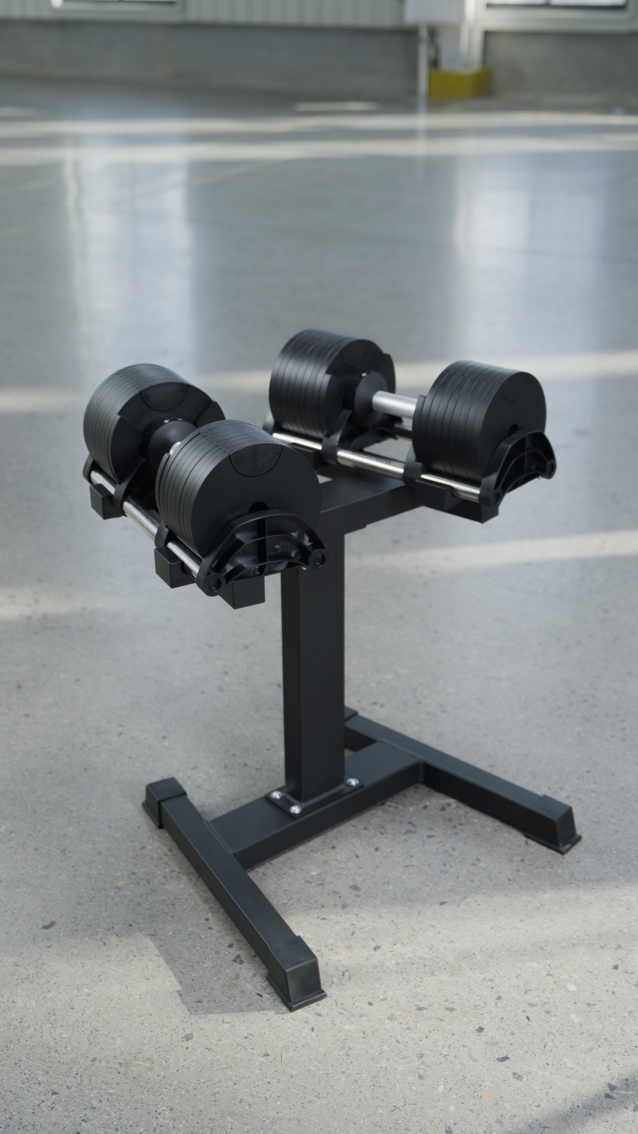 The BefitNow Canada 90lbs Adjustable Cast Iron Dumbbell Pair on a metal stand sits in a bright room with a smooth, light gray floor—an ideal, space-saving addition to any home gym setup.