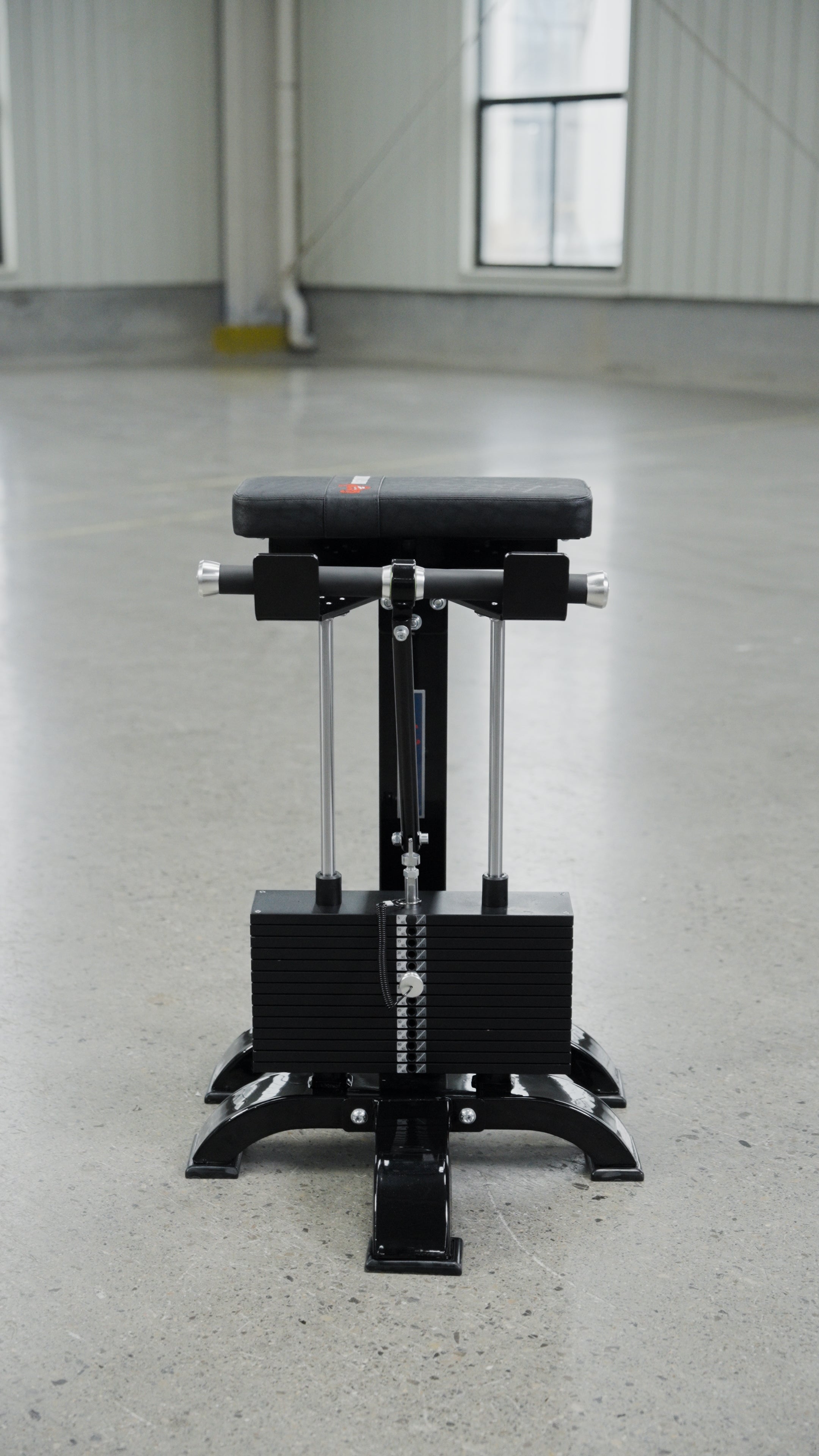 The BefitNow Canada Forearm Trainer, an affordable selectorised machine with a padded seat and adjustable weights, stands on a polished concrete floor in an empty industrial-style room with large windows.