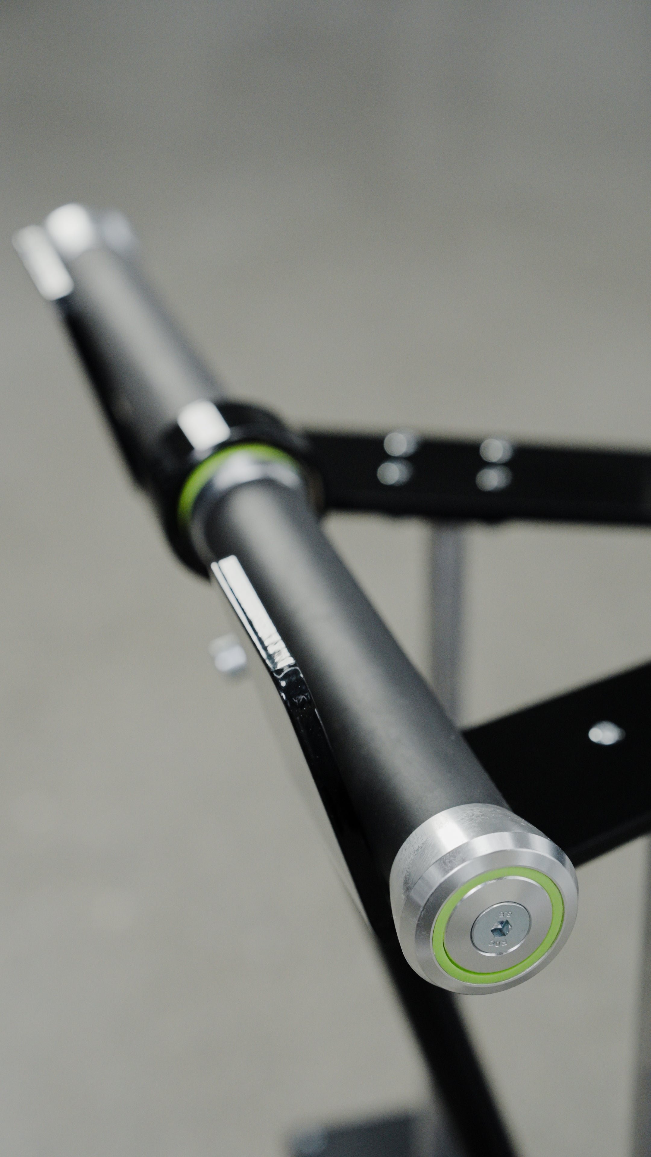 Close-up of the BefitNow Canada Forearm Trainer, an affordable black and silver barbell with green accents, mounted on a black rack against a blurred gray background.