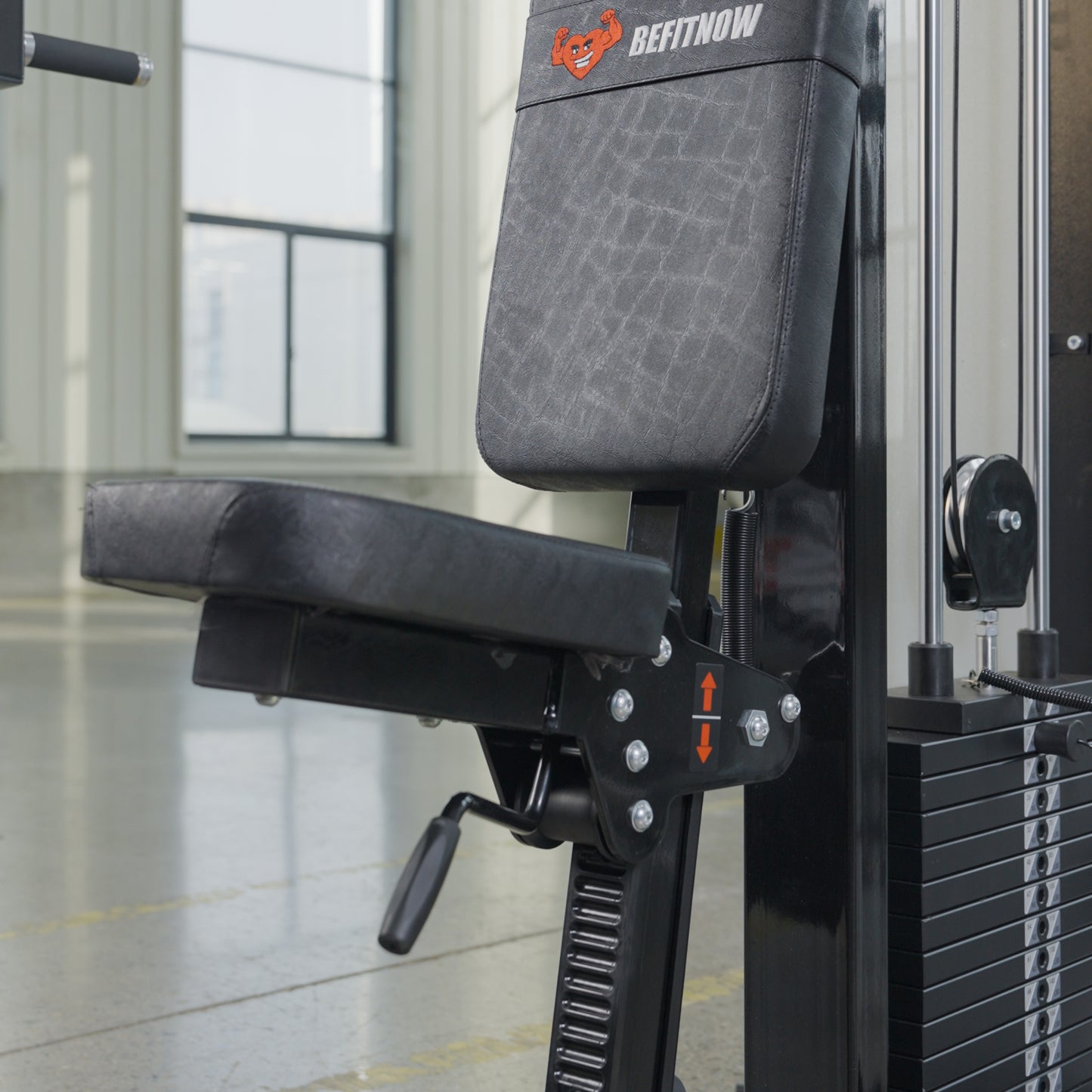 A close-up of a BefitNow Canada Pearl Delt/Pec Fly machine shows its padded seat, backrest, adjustment levers, and weight stack. This dual-function gym equipment is positioned by large windows with natural light streaming in.