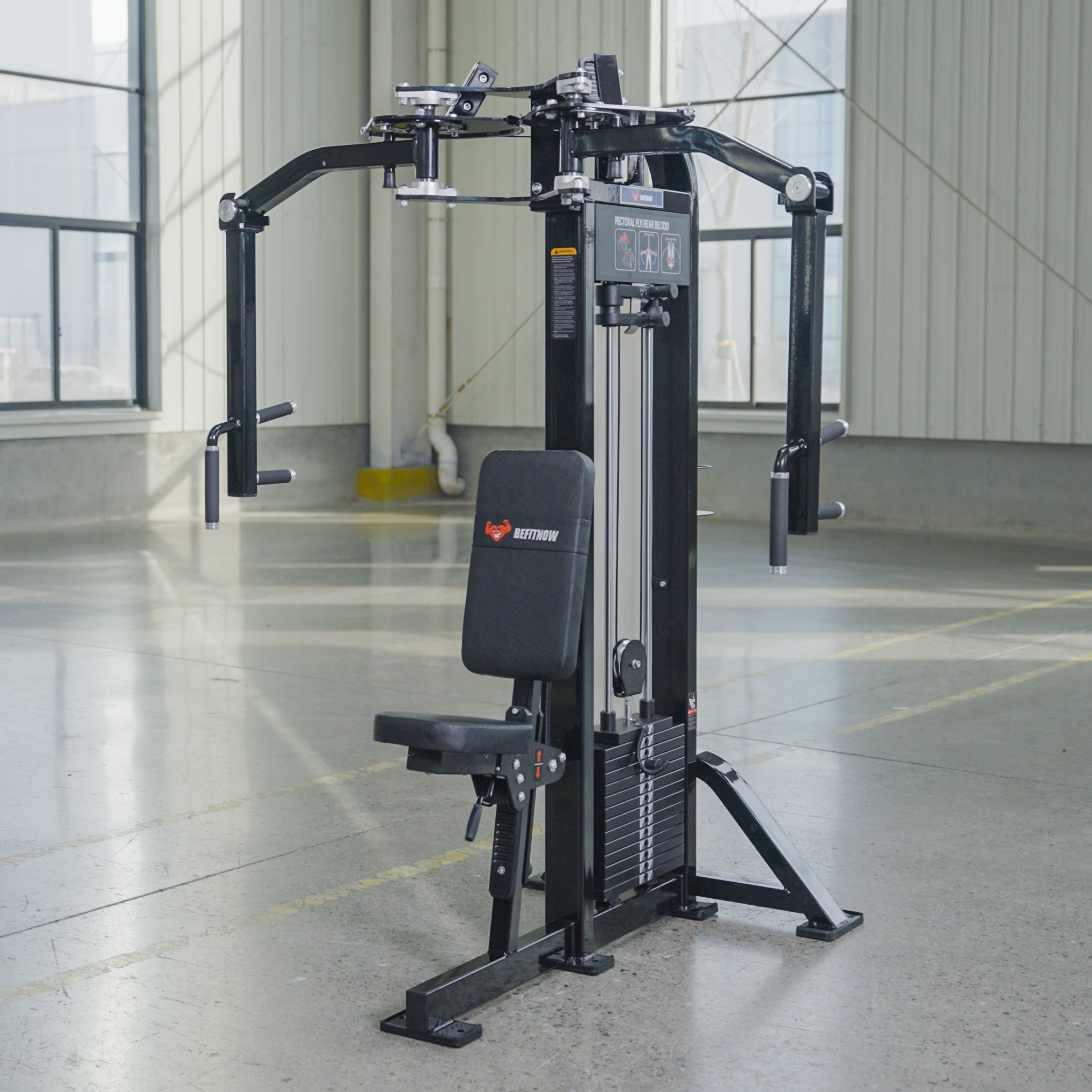 The BefitNow Canada Pearl Delt/Pec Fly is a black dual-function gym machine with padded seat and backrest, adjustable arms, and weight stack, set in a spacious fitness area with large windows and concrete flooring.