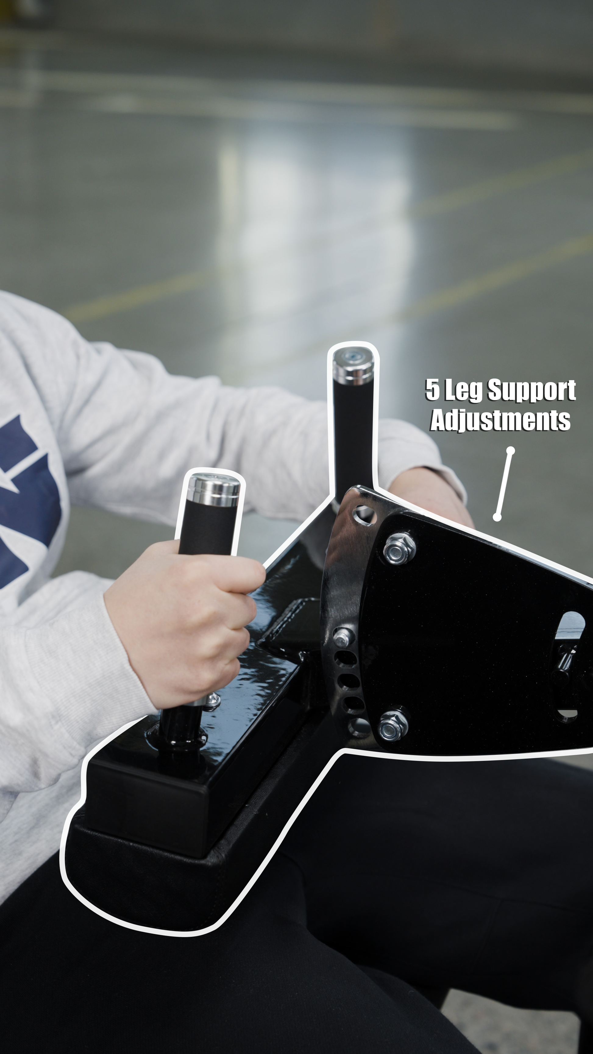 A person in a gray sweatshirt adjusts two black and silver handles on the BefitNow Canada Dual Function Leg Extension Leg Curl Machine, featuring 5 Leg Support Adjustments. The background is a blurred indoor space.