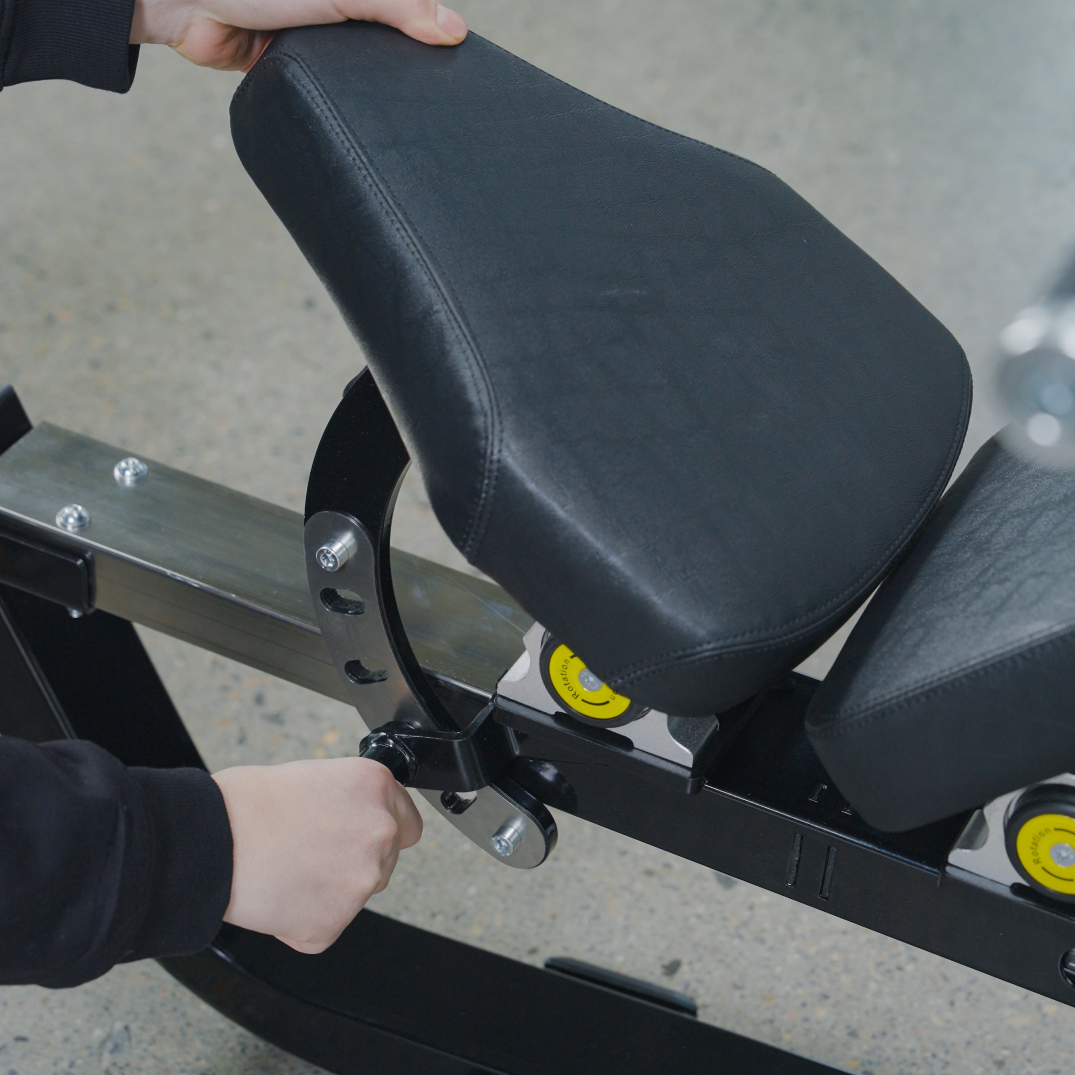 A user adjusts the BefitNow Canada Shoulder Press/Seated Chest Press by turning a lever beneath its black padded seat, showcasing the machine’s user-friendly design. The scene is set against a speckled gym floor.