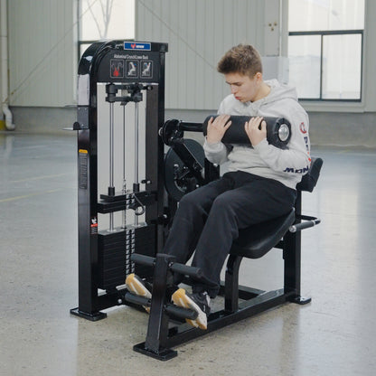 A person in a light gray hoodie and dark pants uses the BefitNow Canada Abdominal Crunch/Low Back machine in a bright, spacious gym with large windows and polished concrete floors, focusing on core strength.