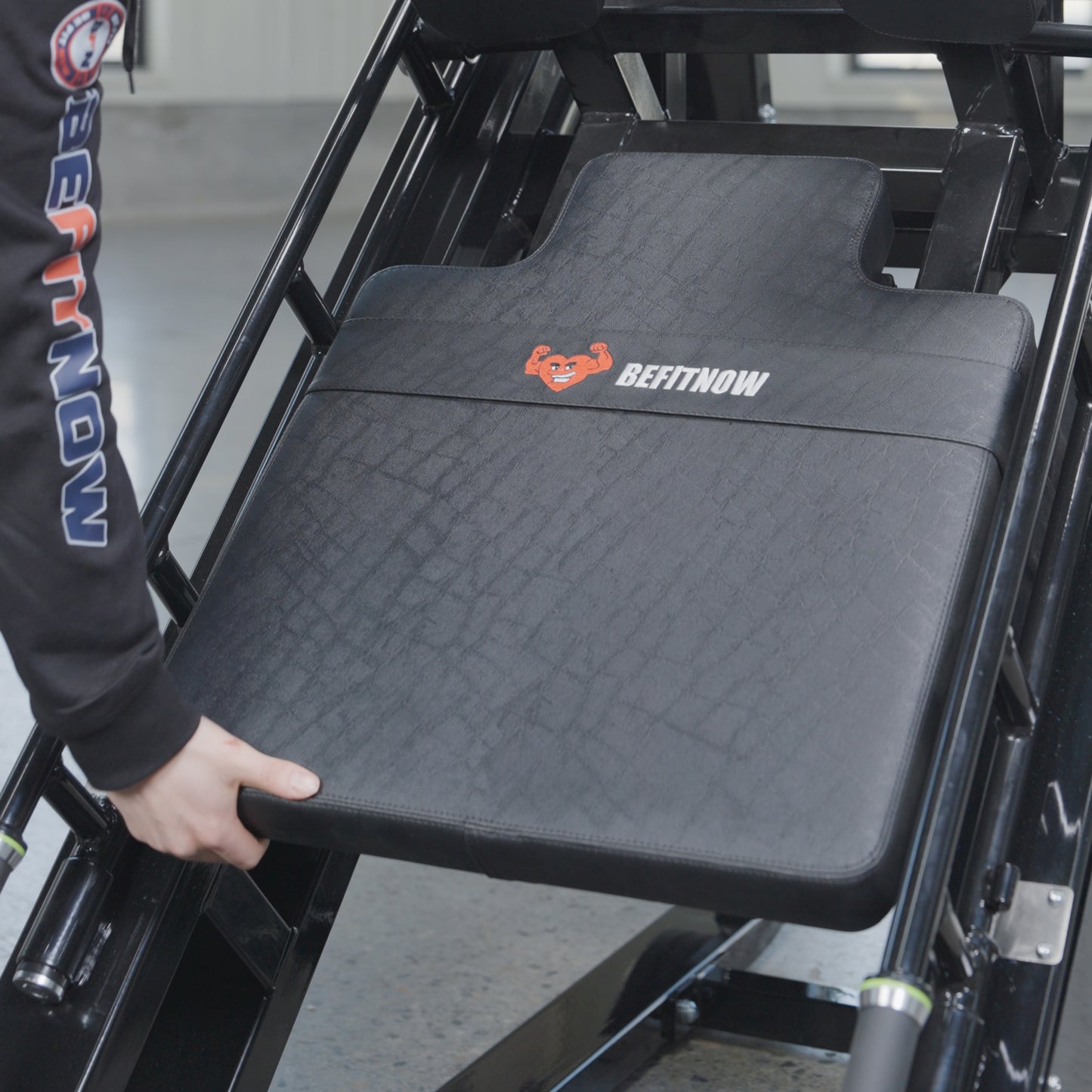 A person adjusts the padded backrest of a BefitNow Canada 45 Degree Leg Press Hack Squat, gripping the edge. The black machine features visible metal frames, measures 93"x65"x57", and weighs 560 lbs.