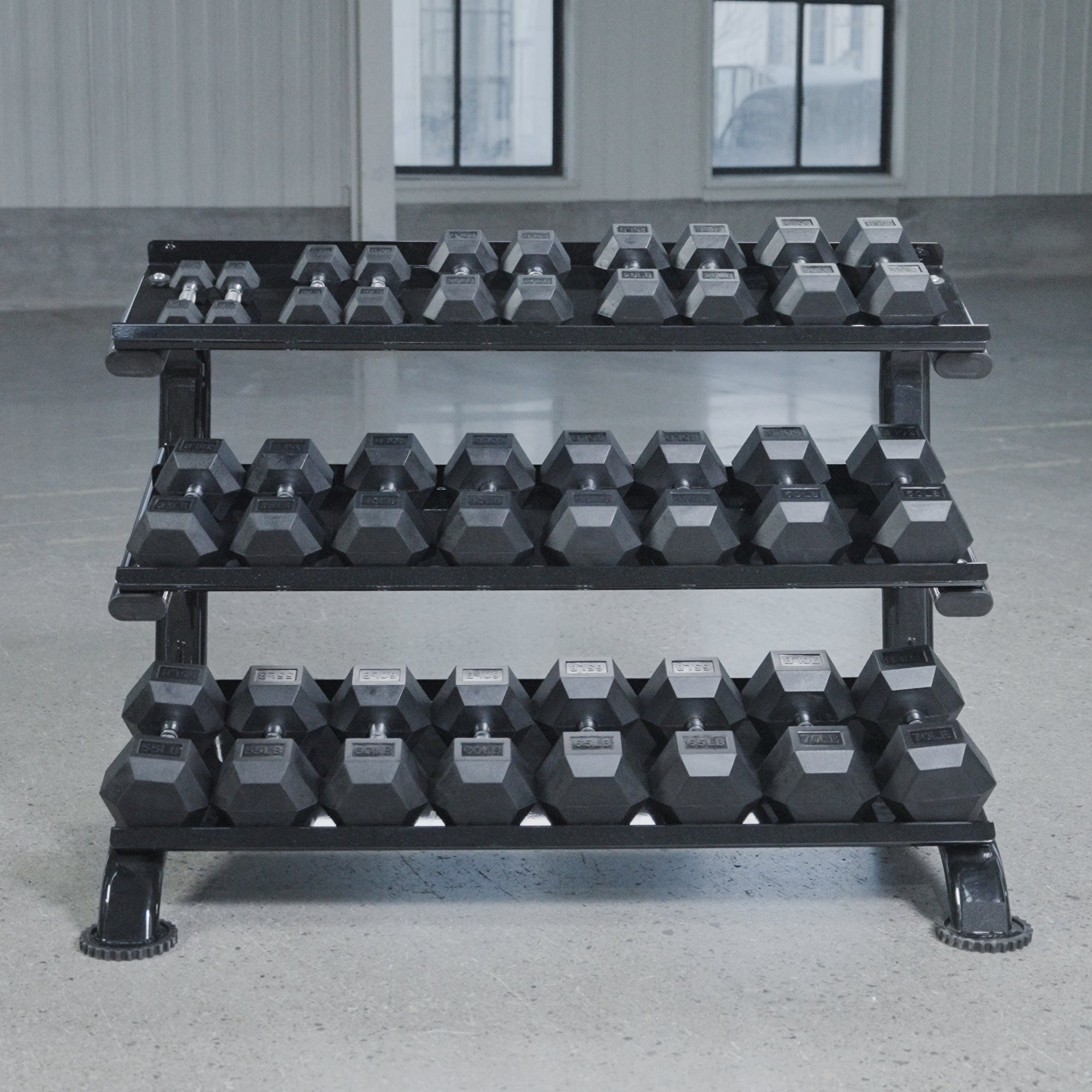The BefitNow Canada 3 Tier Commercial Hex Dumbbell Rack, loaded with black hex dumbbells, stands on a gray gym floor with large windows, offering efficient organization for your workout space.