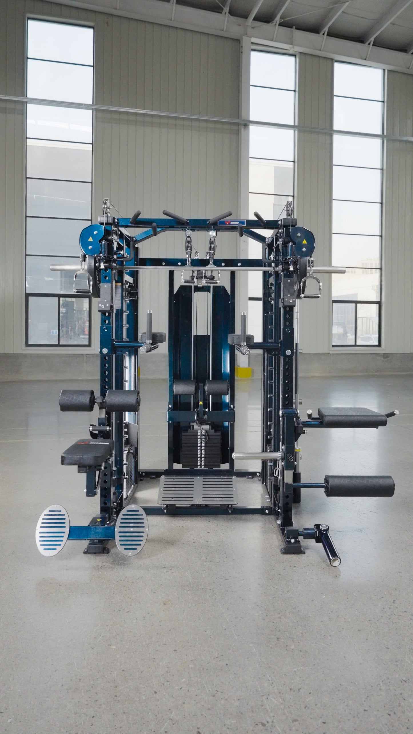 The Professor by BefitNow Canada is a multifunctional gym machine with multiple attachments and pulleys, standing in a spacious, well-lit room with large windows and a high ceiling.