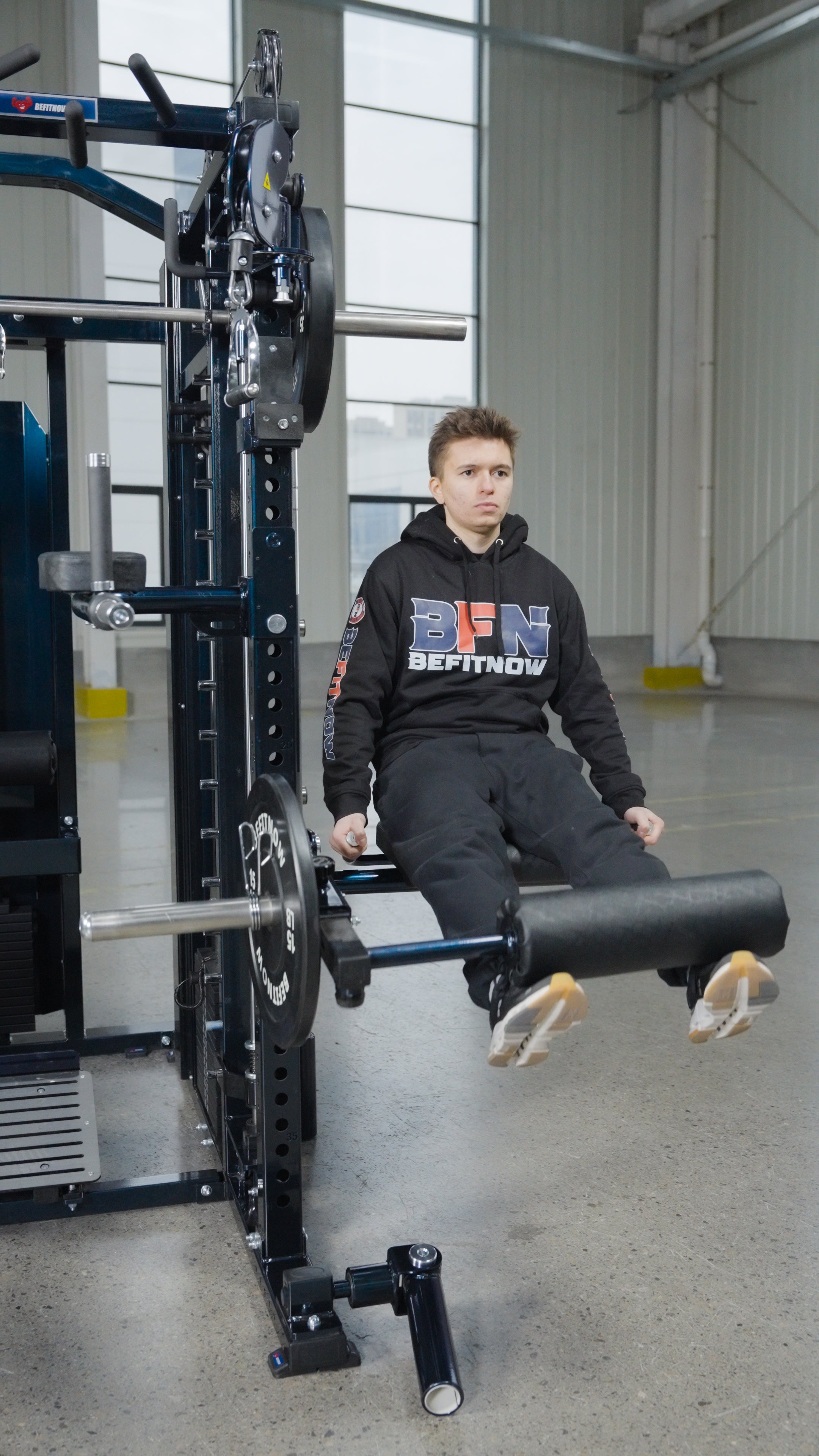 A person in black athletic wear uses BefitNow Canada's The Professor: The Kahuna on Steroids leg extension machine at the gym, lifting the padded bar with their legs while seated upright and looking forward.