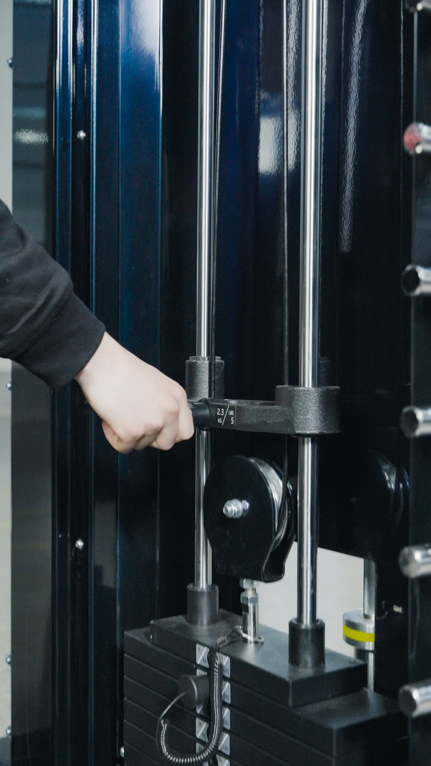 A person adjusts the weight stack on BefitNow Canada's The Professor by inserting a pin into the desired level. This functional trainer features metal rods and black plates, making it versatile home gym equipment.