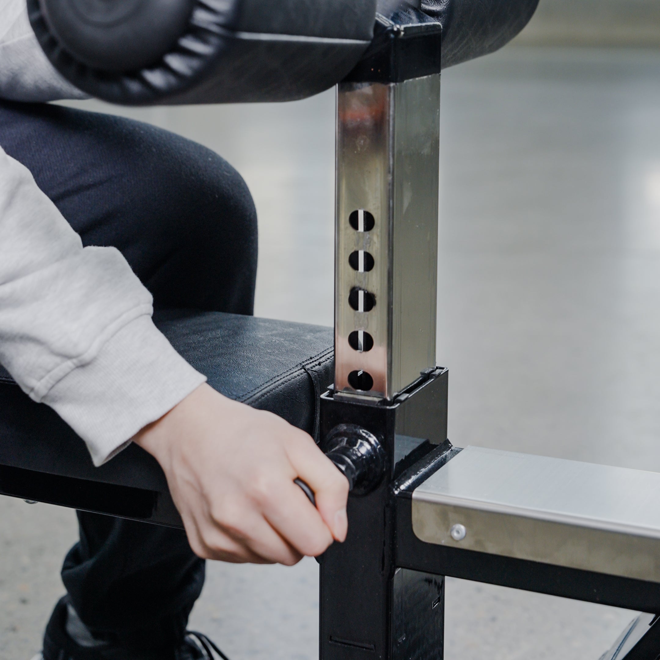 A person adjusts the height of the BefitNow Canada Lat Pulldown/Low Row by turning a knob on its metal support, surrounded by other Commercial Gym Equipment, while wearing a white sleeve and black pants.
