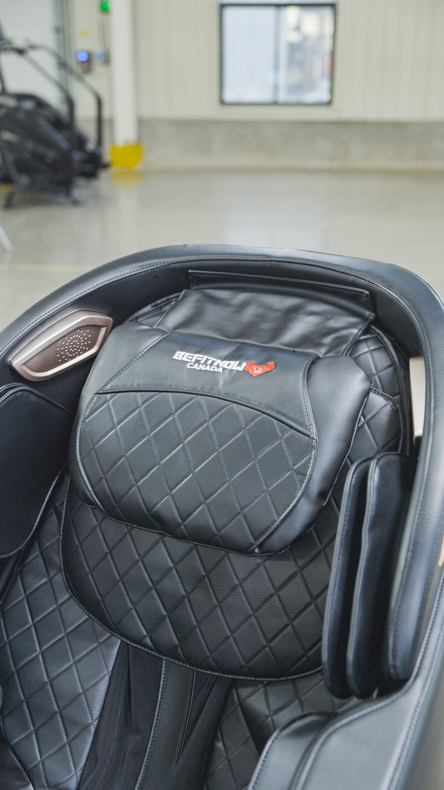 Close-up of the BefitNow Canada SL Full Body Commercial Massage Chair in black quilted leather, featuring a red emblem on the headrest and offering a 3D massage experience, displayed indoors on a smooth floor.