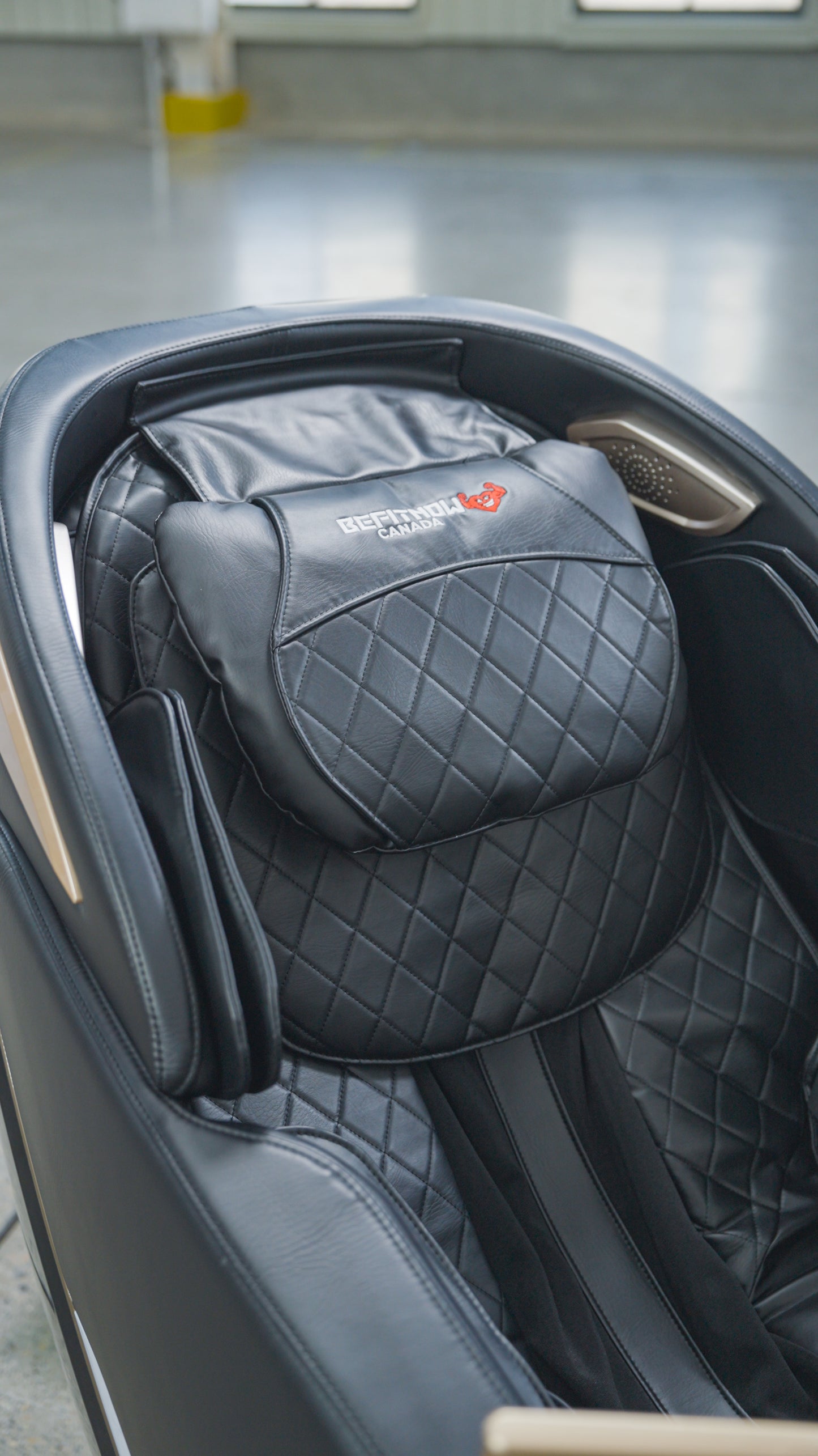Close-up of the BefitNow Canada SL Full Body Commercial Massage Chair featuring quilted black leather padding and a branded headrest, placed in a bright indoor space with a concrete floor.