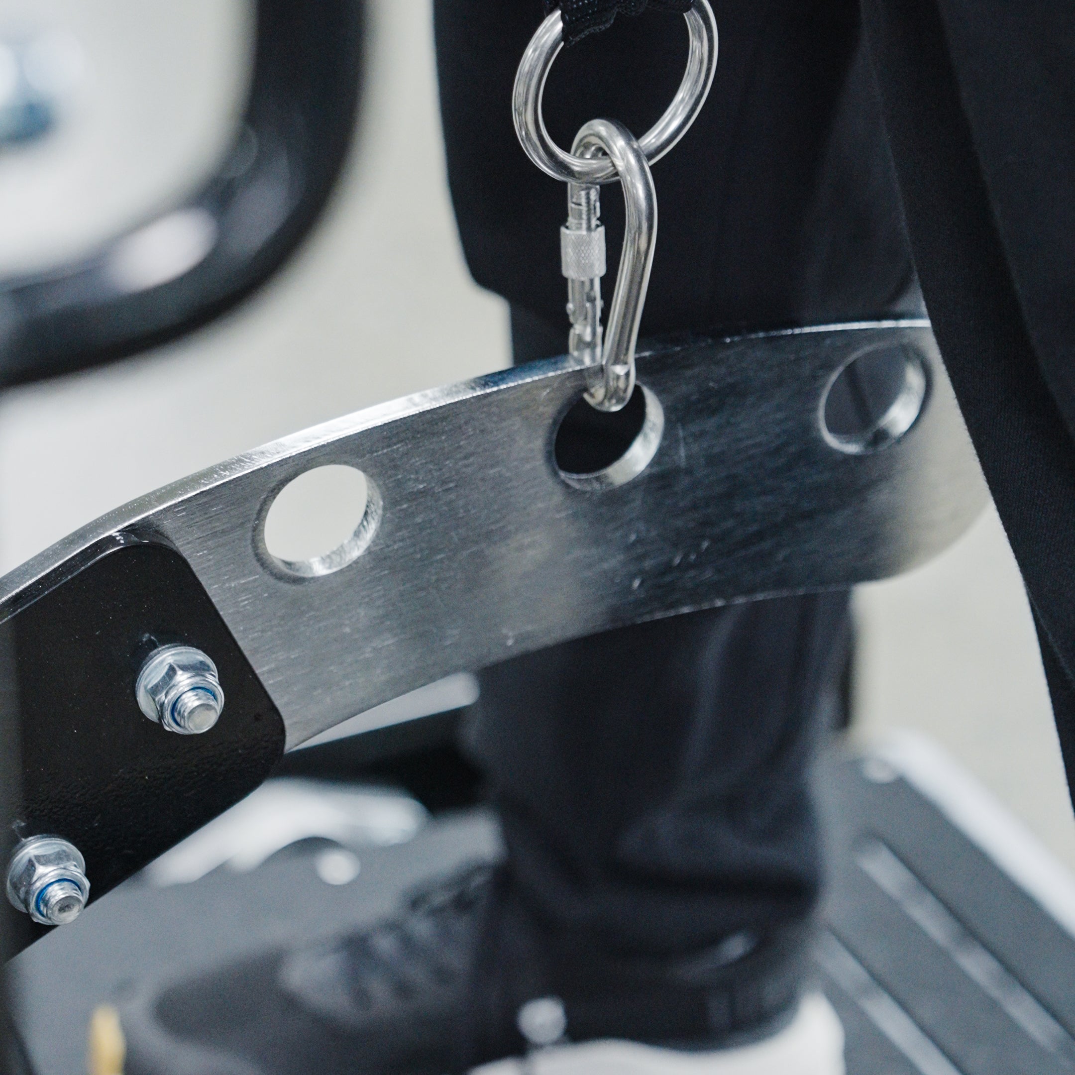 A close-up of the BefitNow Canada Commercial Belt Squat Trainer’s metal bar with circular holes, secured by bolts and a carabiner. A person in black pants and shoes stands on a platform nearby.