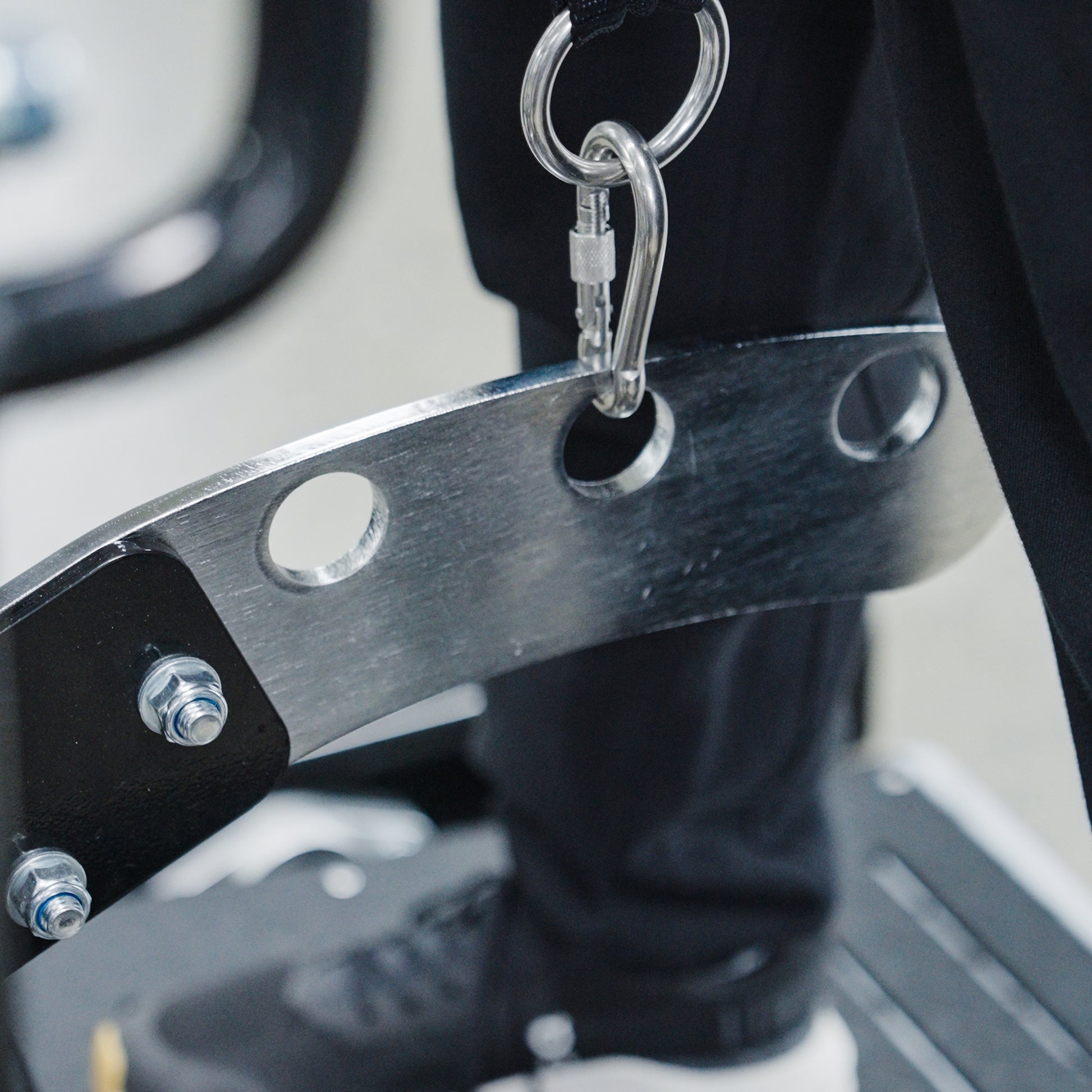 A close-up of the BefitNow Canada Commercial Belt Squat Trainer’s metal bar with circular holes, secured by bolts and a carabiner. A person in black pants and shoes stands on a platform nearby.