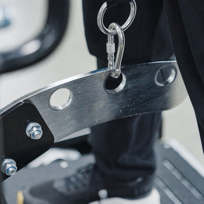 A close-up of the BefitNow Canada Commercial Belt Squat Trainer’s metal bar with circular holes, secured by bolts and a carabiner. A person in black pants and shoes stands on a platform nearby.