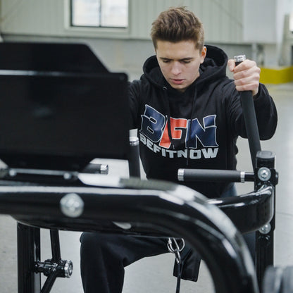 A young man wearing a BefitNow Canada hoodie uses the Commercial Belt Squat Trainer in a gym, focusing intently on his workout.