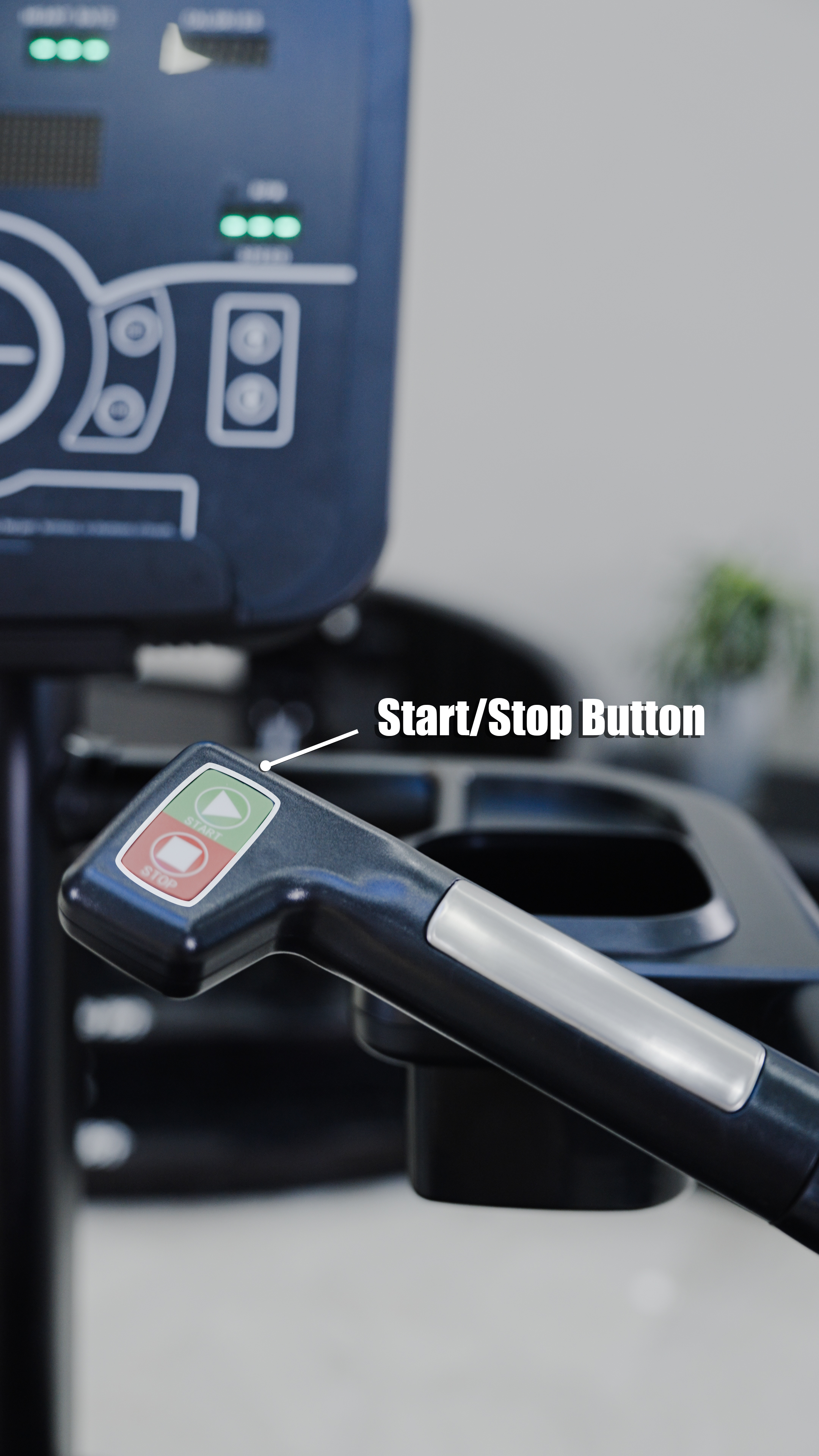 Close-up of a black handle with green start and red stop buttons labeled "Start/Stop" and an arrow. The BefitNow Canada Stair Climber 3000 - The Peak Punisher is blurred in the background, along with a plant.