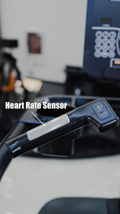 Close-up of a treadmill handle with a silver heart rate sensor and control buttons. In the background, a blurred BefitNow Canada Stair Climber 3000 – The Peak Punisher, featuring joint-safe climbing technology, is visible.