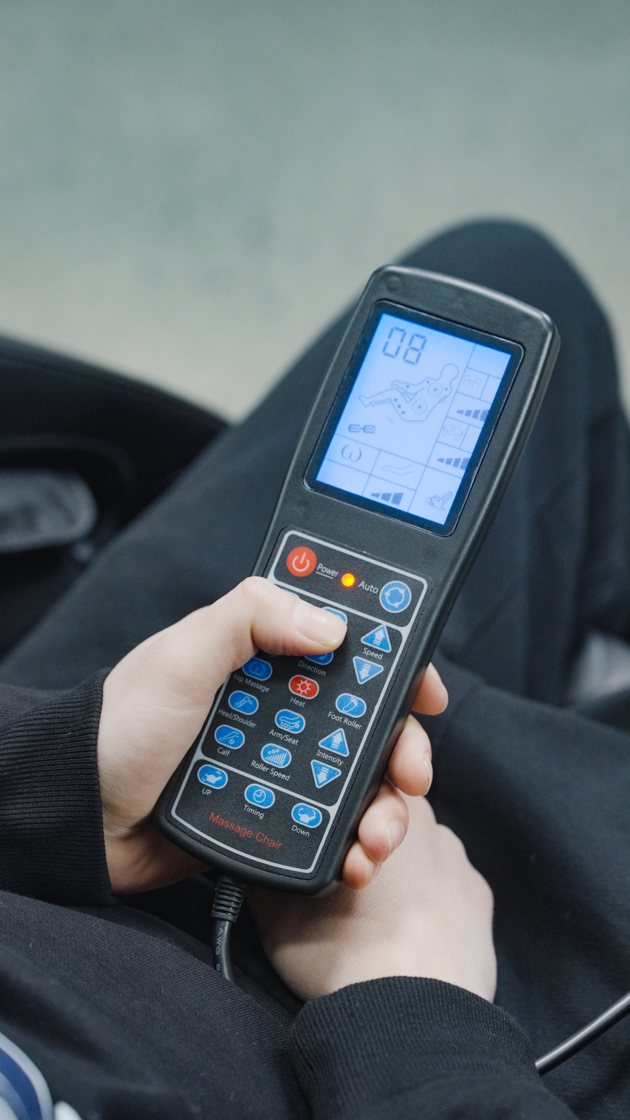Clad in dark attire, someone uses a remote with a screen displaying settings and buttons to adjust the BefitNow Canada Luxurious Zero Gravity Massage Chair, their thumb pressing a button to control its advanced comfort features.