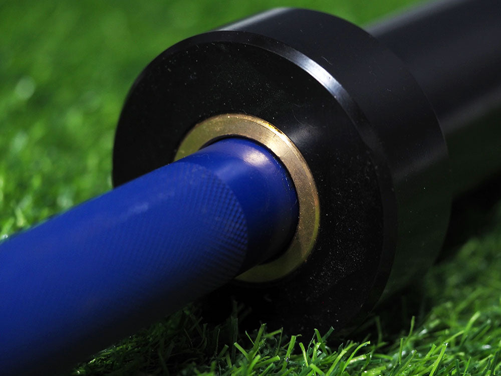 A close-up of a blue, textured-grip Custom Barbells shaft and black sleeve with a metallic ring lies on bright green grass, perfectly capturing the vibrant detail and quality of BefitNow Canadas Olympic barbells.