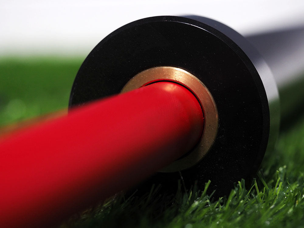 A close-up of BefitNow Canadas Custom Barbells resting on green artificial turf shows the black end encircled by a metallic gold ring, creating a striking contrast with the vibrant textures.