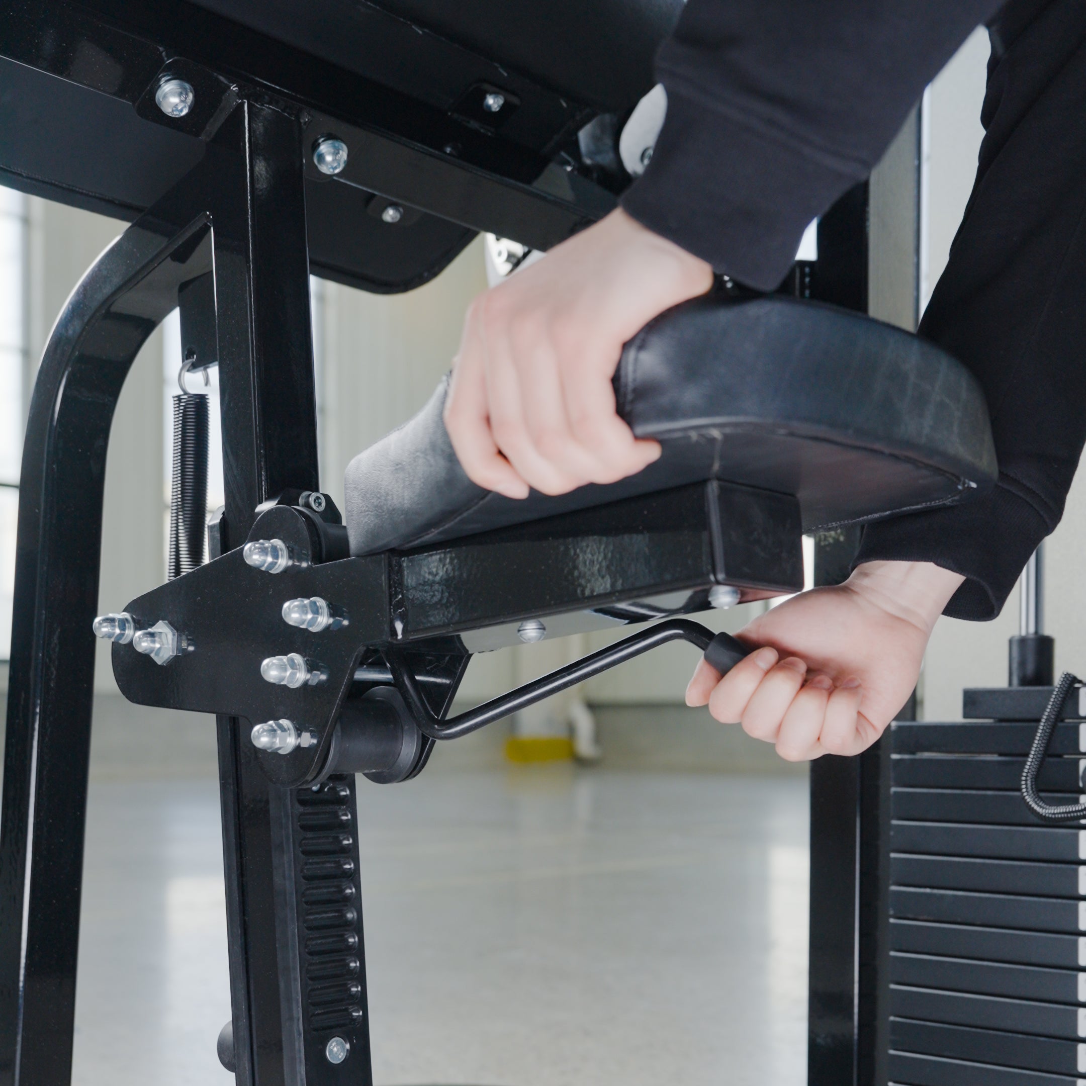 A user adjusts the seat height of the Dual Function Biceps/Triceps by BefitNow Canada, pulling a lever while gripping the seat and handle. The sturdy metal frame, weight stack, and adjustable resistance are visible.