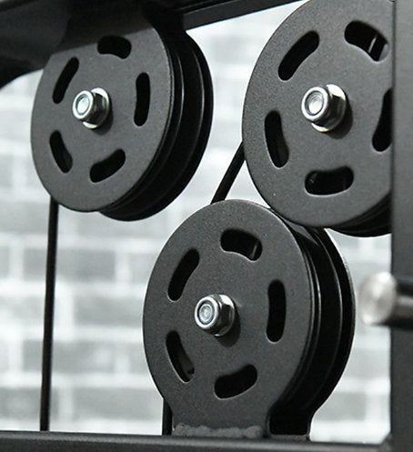 A close-up shows three black grooved pulleys mounted in a metal frame, similar to those on the BefitNow Canada Heavy Duty Smith Machine. The backdrop is a slightly blurred gray brick wall.