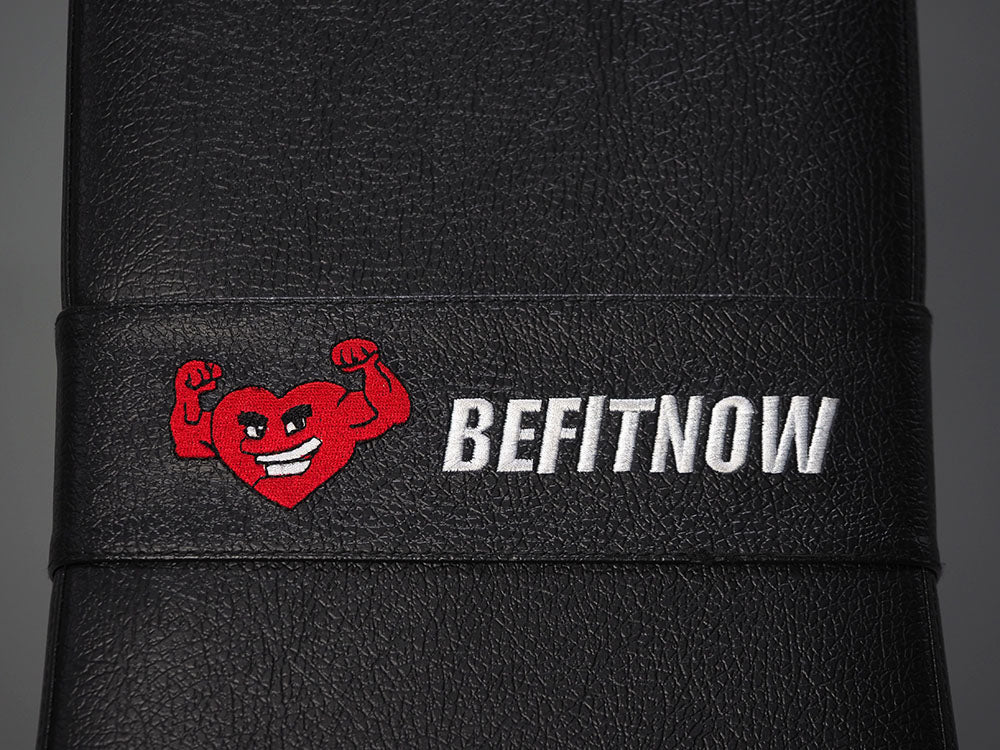 A black surface showcases a smiling red heart flexing biceps with BEFITNOW in white, echoing the strength of the TM87 Fully Adjustable Commercial Bench by BefitNow Canada, made from 11-gauge steel.