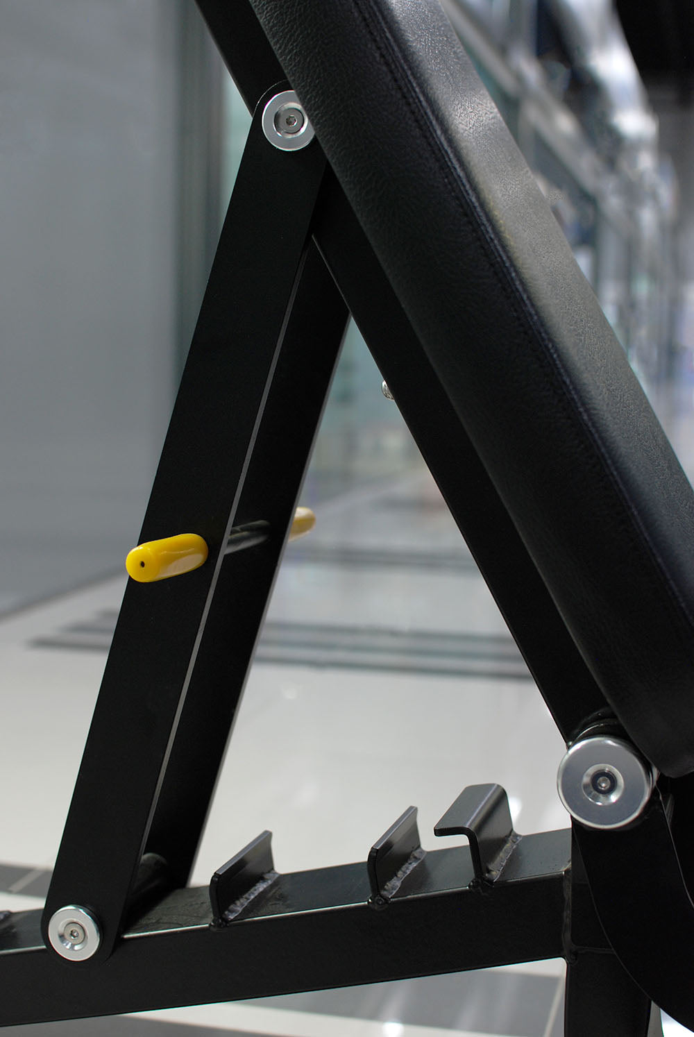 Close-up of the TM87 Fully Adjustable Commercial Bench by BefitNow Canada, highlighting its incline adjustment mechanism. The custom-built bench includes a yellow pin and multiple notches for angle settings, set against a blurred gym interior.